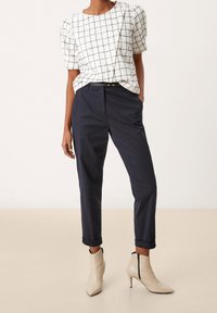 Bílý top s námořnickou kostkou a balónovými rukávy, doplněný tmavě námořnickými kalhotami a béžovými špičatými kotníkovými botami se zipy.