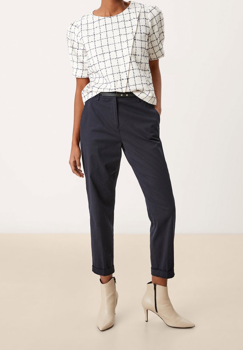 Bílý top s námořnickou kostkou a balónovými rukávy, doplněný tmavě námořnickými kalhotami a béžovými špičatými kotníkovými botami se zipy.