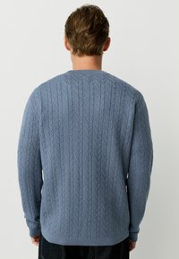 Light blue knitted sweater featuring a cable pattern, crew neck, ribbed cuffs, and hem. The back view shows a textured design.