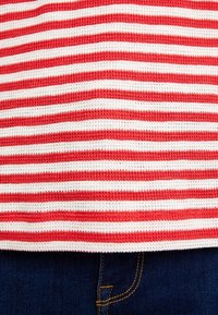 Rot-weiß gestreiftes gestricktes Top mit einer gerippten Struktur und lockerem Schnitt, getragen über dunkelblauen Jeanshosen.