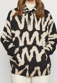 Bluza z kapturem w kolorze kremowym i czarnym, z motywem zygzaka, kaptur na sznurek, kieszeń z przodu oraz ściągacze na rękawach. Miękka tekstura materiału.