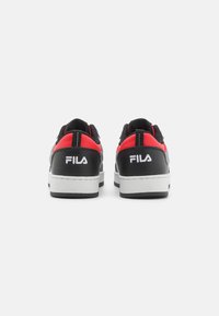 Zapatillas negras y rojas con una parte superior sintética texturizada, detalles blancos y una suela de goma gruesa. Cuenta con una lengüeta en el talón.