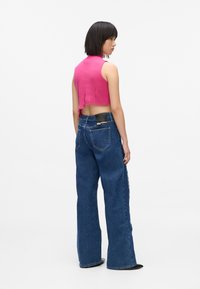 Růžový cropped top s obroušenými okraji v úzkém střihu, zkombinovaný s modrými denimovými kalhotami širokého střihu s vysokým pasem a černou nášivkou na zadní straně.