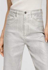 Hochtaillierte silberne Jeans verfügen über eine glatte, glänzende Textur mit Fronttaschen und einem Knopfverschluss. Erhältlich im geraden Bein-Design.