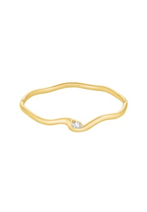 Anillo ondulado de oro con una pequeña gema clara en forma de lágrima situada en el centro, diseño minimalista y elegante sobre fondo blanco.