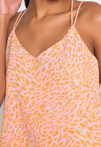 Roze mouwloze blouse met een V-hals, met een oranje en lichtblauw abstract patroon en dunne bandjes. Zachte stof met een lichte glans.