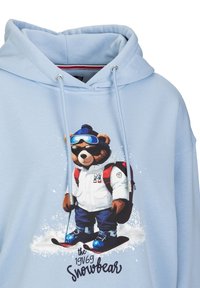Lichtblauw hoodie met een cartoon beer in skikleding, met een witte jas, blauwe accenten en skiën op sneeuw. Voorzijde met grafisch ontwerp.