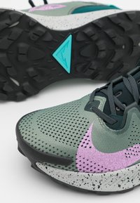 Chaussure de trail running verte et violette avec une tige en mesh texturé, un col de maintien et une semelle intermédiaire grise tachetée. Semelle extérieure en caoutchouc noir durable.