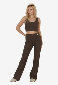 Brązowy prążkowany crop top i dopasowane spodnie dzwony. Posiada szeroki pas z ozdobnym akcentem. Wykonane z miękkiego, elastycznego materiału.