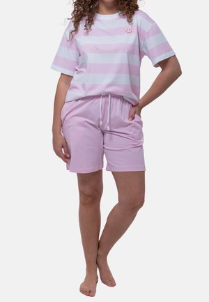 Kvinde iført lyserød og hvidstribet t-shirt med smiley og matchende lyserøde shorts med snøre, stående barfodet.