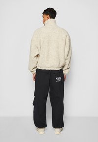 Kremfarget faux fur-jakke med høy krage, kombinert med løstsittende svarte cargo-bukser med hvit logodetalj og sidelommer.