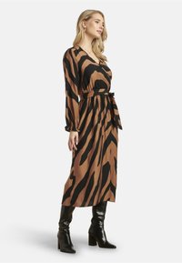 Bruin en zwart gestreepte midi-jurk met een taille die is aangesnoerd en lange mouwen; gecombineerd met zwarte hoge hakken. Zacht materiaal met een vloeiende uitstraling.