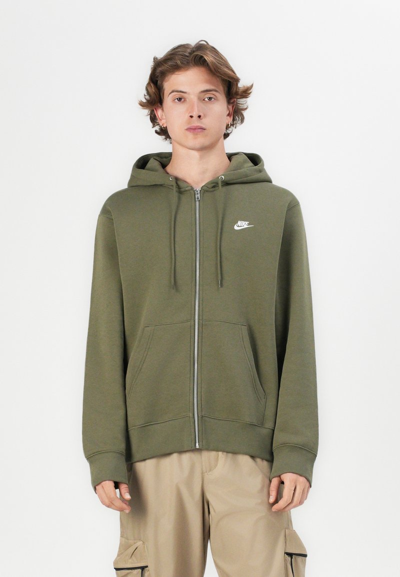 Sweatshirt verde-azeitona com fecho lamado, em tecido suave, apresentando um zíper frontal, bolsos laterais e um pequeno logo branco da Nike no peito.