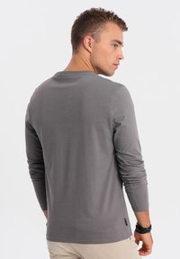 Graues Langarm-T-Shirt aus weichem Material, mit Rundhalsausschnitt, schmaler Passform und dezentem Logodetail am Saum.