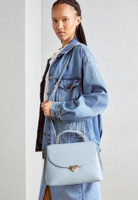 Bolso de mano de cuero azul claro con una forma estructurada, que cuenta con un cierre en forma de triángulo con acento dorado y una correa de hombro ajustable.