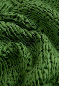 Gros plan sur un tissu vert tricoté texturé avec un motif tissé épais et une surface douce et pliée.