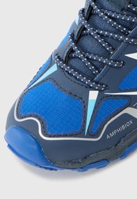 Chaussure de sport bleue en matériau mesh et synthétique. Présente des accents réfléchissants, un tissu texturé et une semelle en caoutchouc robuste. Les lacets sont foncés avec des pois blancs.