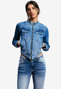 Teksasti jope lühem disainiga, kõrge kaeluse, kahe rinnatasku ja tõmblukuga. Hele sinine värv kulunud tekstuuriga.