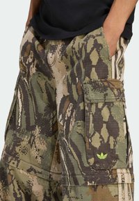 Pantalones cortos cargo en un patrón de camuflaje con tonos de verde y marrón. Presentan bolsillos laterales y un pequeño logo verde cerca del bolsillo.