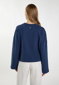 Granatowy, oversize'owy sweter z okrągłym dekoltem, wydłużonymi rękawami i małym logo na plecach. Miękka tekstura, luźny krój.
