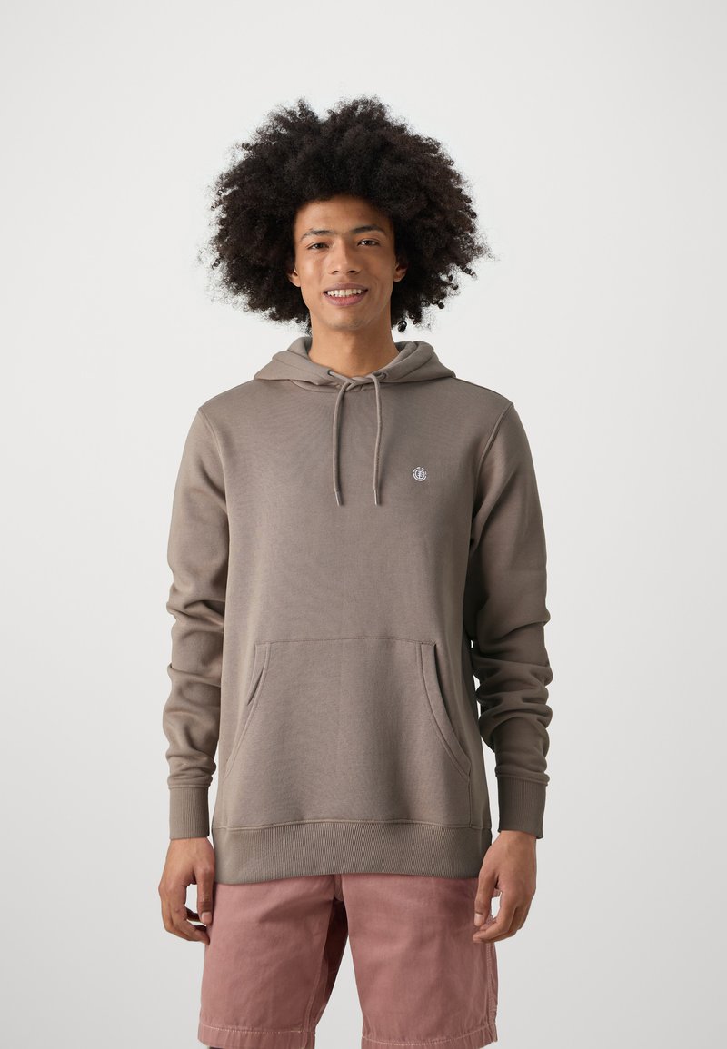 Bruine sweatshirt met een capuchon, kangoeroezak en ribgebreide mouwen. Heeft een klein logo op de borst. Gemaakt met lichtroze shorts.
