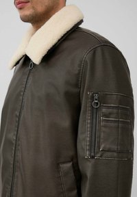 Braune Lederjacke mit einem cremefarbenen Schafslederkragen, seitlichem Reißverschlussfach und strukturierten Details an den Ärmeln.