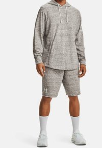 Grauer, strukturierter Kapuzenpullover mit einer Kängurutasche, kombiniert mit passenden Shorts. Zeigt das Under Armour-Logo in Hellgrau. Weiße Sportsocken und Schuhe.