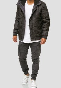 Svart vadderad jacka med fleece-fodrad krage och flera fickor, i kombination med grå cargobyxor och vita sneakers. Avslappnad look.