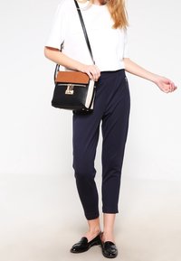Black and tan handbag with a gold buckle, paired with a white top and navy tapered pants. Smooth textures and clean lines are featured.