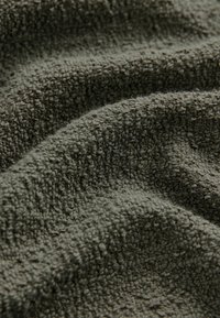 Tissu de couleur vert olive texturé avec une surface douce et duveteuse, présentant un motif de tissage en boucle et des variations subtiles de couleur et de profondeur.