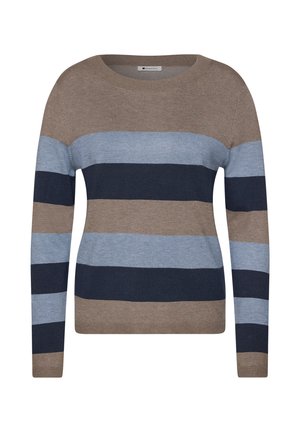 Femme aux cheveux bruns mi-longs sourit doucement, portant un pull en laine rayé marron, bleu clair et bleu foncé sur un fond uni.