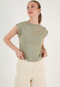 Oliven grøn kortærmet t-shirt med en afslappet pasform og rund hals, parret med lysebeige bukser; glat tekstur og minimalistisk design.