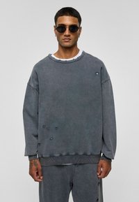 Grijze oversized sweatshirt van katoen, met beschadigde details, een ronde halslijn en geribbelde manchetten. Gekocht met een wit ondershirt.