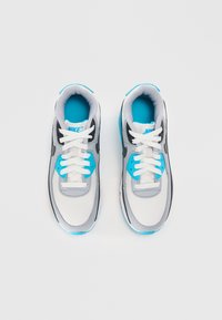 Nike tenisice s kombinacijom bijele, sive i crne boje. Imaju akcentne detalje u tirkiznoj boji, teksturirani mrežasti jezik i bijele vezice.
