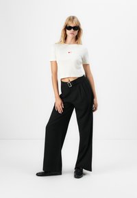Vitt kort t-shirt med röd hjärt-design, matchat med svarta högmidjade vida byxor och svarta skor. Minimalistisk och modern stil.