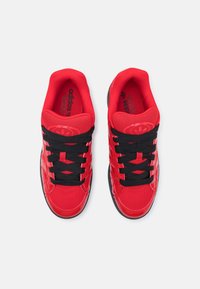 Punaiset urheilukengät, joissa on verkko- ja synteettinen päällinen, mustat nauhat, pyöreä kärki, pehmustettu kaulus ja kuvioitu pohja. Logo kielekkeessä.