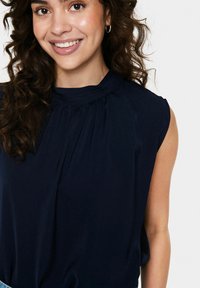 Top senza maniche di colore blu navy con scollatura a girocollo, caratterizzato da cuciture arricciate sulle spalle e una texture del tessuto liscia.