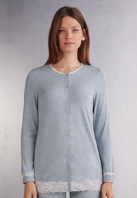 Lichtblauwe lange mouwen cardigan met een ronde halslijn, voor knopen en witte kantafwerking aan de onderrand. Zachte stof met een gestructureerde uitstraling.