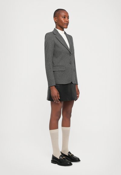 Grijze textuur blazer met één knoop, gecombineerd met een zwarte leren mini-rok, beige kniekousen en zwarte instapschoenen.