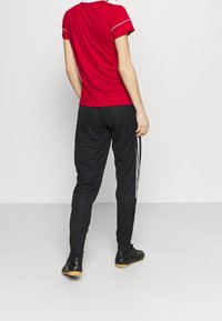 Red t-shirt with white trim, paired with black pants featuring white side stripes. Material appears athletic and lightweight.