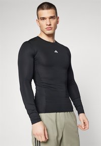 Zwart longsleeve sportshirt met een ronde hals, gemaakt van rekbaar materiaal, met een klein wit logo op de borst.