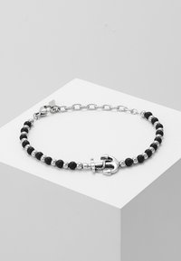 Pulsera de cuentas negras con charm en forma de ancla de plata, alternando cuentas brillantes y eslabones de cadena. Textura suave con acentos brillantes.