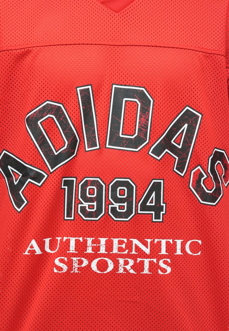 Maillot de sport rouge en tissu perforé, avec un grand texte noir "ADIDAS 1994" et un texte blanc "AUTHENTIC SPORTS" sur la poitrine.