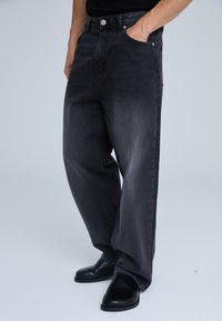 Jeans in denim nero dal taglio oversize, con chiusura anteriore a bottone, tasche standard e leggera sbiaditura sulla trama del tessuto.