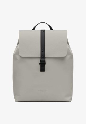Sac à dos gris clair, fabriqué à partir d'un matériau durable. Présente un rabat avant avec une sangle noire et une fermeture à bouton. Design minimaliste.