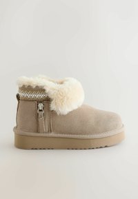 Beige Knöchelstiefel mit einem flauschigen, cremefarbenen Kragen, strukturiertem Wildledermaterial, seitlichem Reißverschluss und einer flachen Gummisohle.