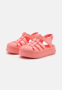 Sandálias cor-de-rosa em coral feitas de material flexível; apresentam bico fechado, calcanhar aberto e detalhes decorativos em nervuras nas tiras.