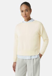 Lichtgele sweatshirt met een ronde hals, ribgebreide manchetten en een subtiele logo-detail op de zoom, gelaagd over een lichtblauw shirt.