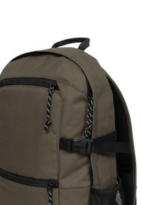 Sac à dos kaki avec des fermetures éclair noires, des sangles réglables et une poche latérale en mesh. Il possède une texture de tissu durable et des cordons de serrage contrastants.