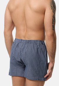 Bóxer a cuadros en navy y blanco con cintura elástica, que presenta un corte holgado y una textura de tela suave, visto desde atrás.